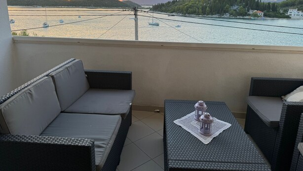 Un balcon agrémenté de meubles en osier, une table avec une lanterne et une vue sur un lac où l’on aperçoit des bateaux et des montagnes.