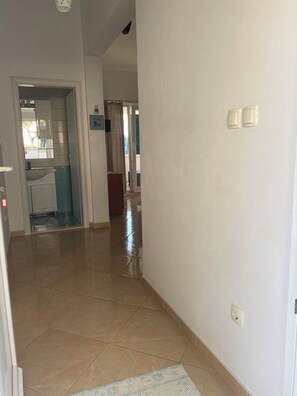 A hallway with a tiled floor, a door leading to a bathroom, and a view of a balcony with a curtain.