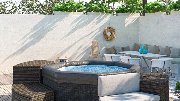 En rund utomhusbubbelpool med sittplatser i rotting och ett bord med kuddar.