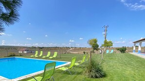 A swimming pool with green chairs, a grassy lawn, and a clear blue sky.