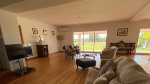A spacious living room with a wooden floor, a large sofa, a television, and a bench.