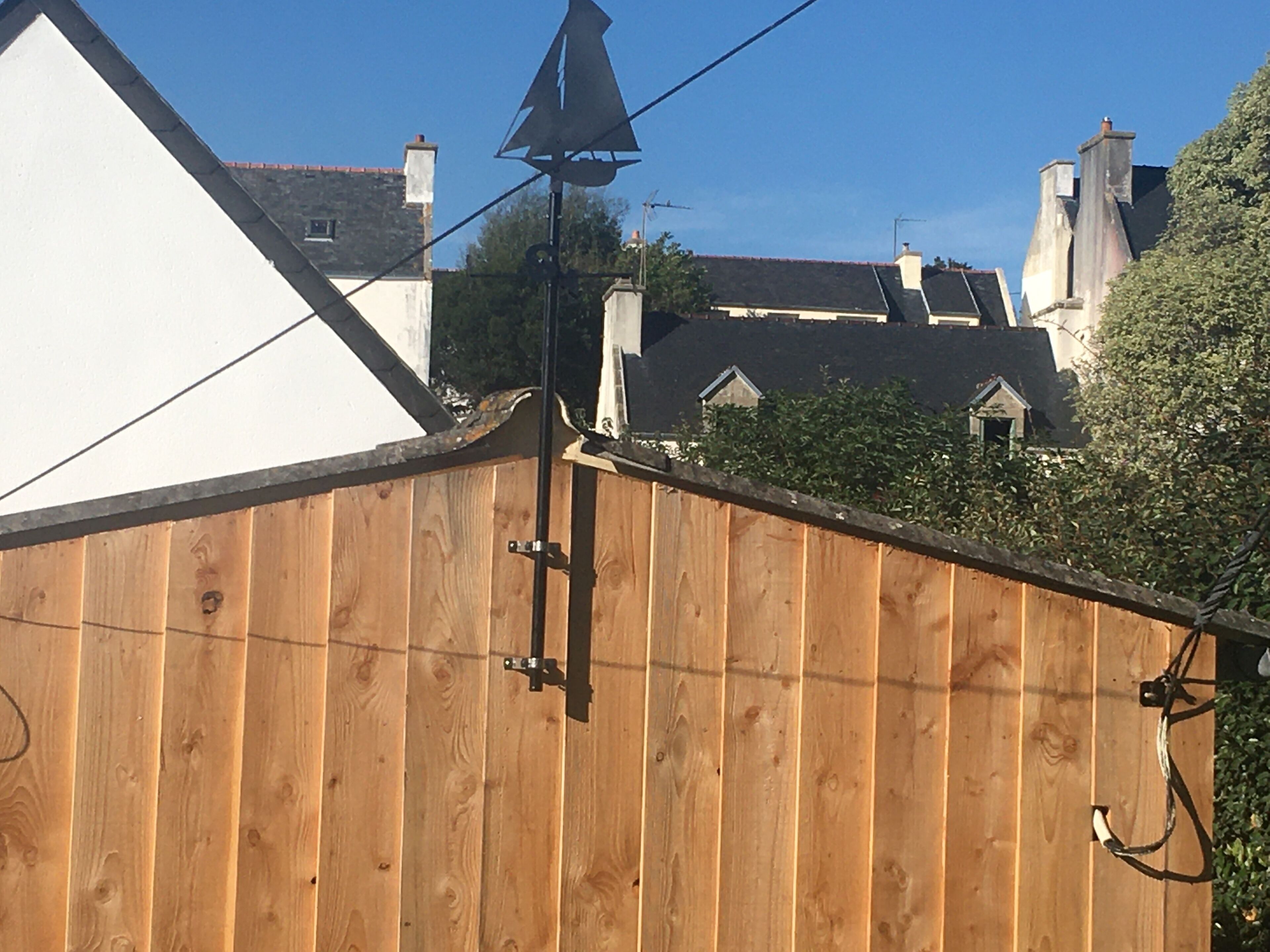 A wooden fence with a metal gate, a triangular roof, and houses in the background.