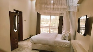 A bedroom with a bed, a mirror, a window with curtains, and a door.
