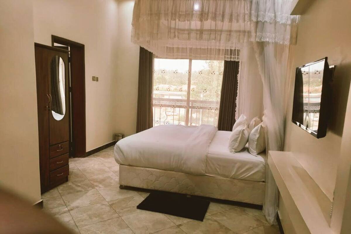 A bedroom with a bed, a mirror, a window with curtains, and a door.
