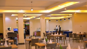 Un restaurante amplio con varias mesas y sillas, una barra con un empleado y un monitor de computadora en la pared.