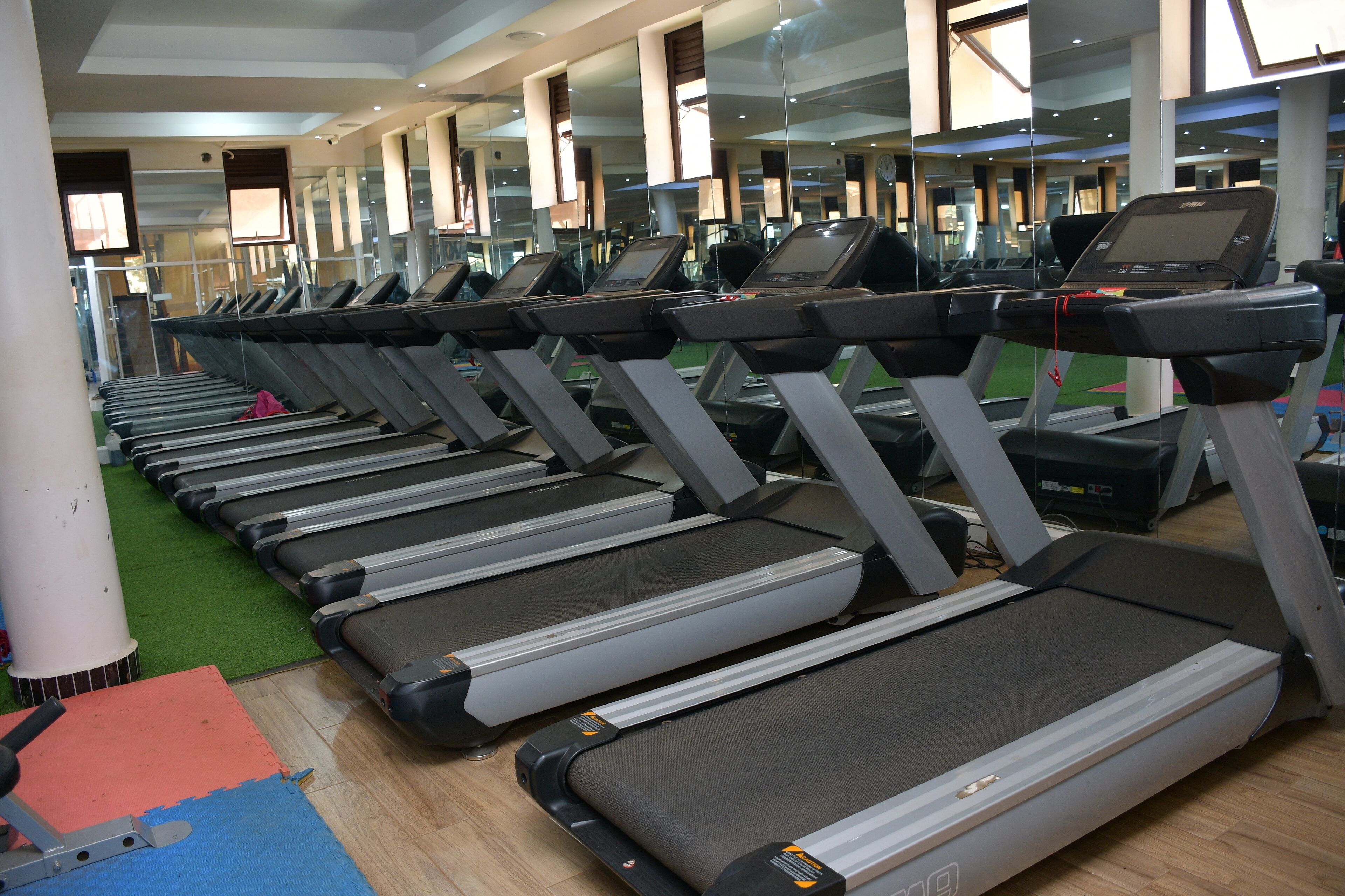 Une rangée de tapis de course dans une salle de sport, les murs étant recouverts de miroirs.