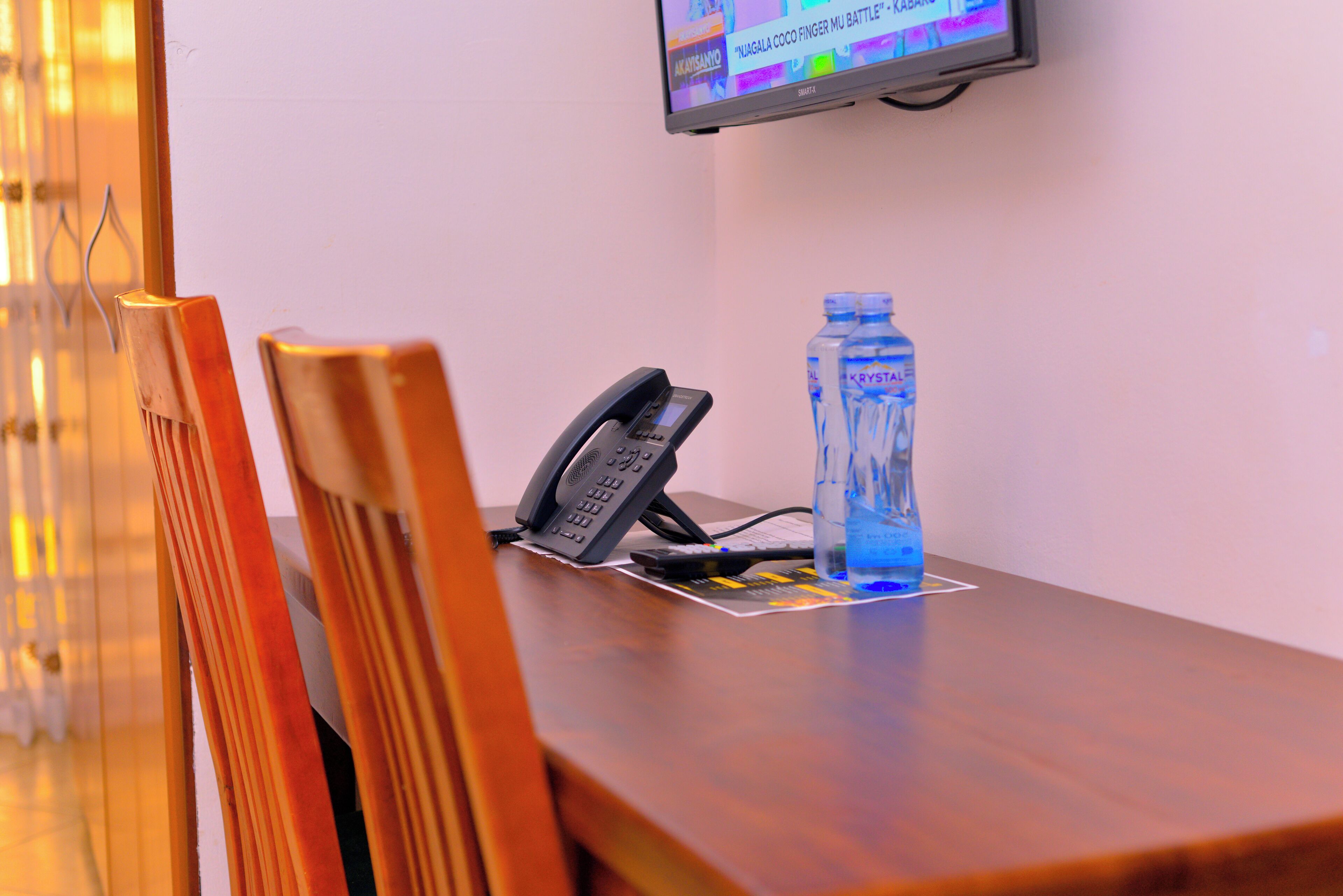 A wooden table with a telephone, a water bottle, and a remote control.