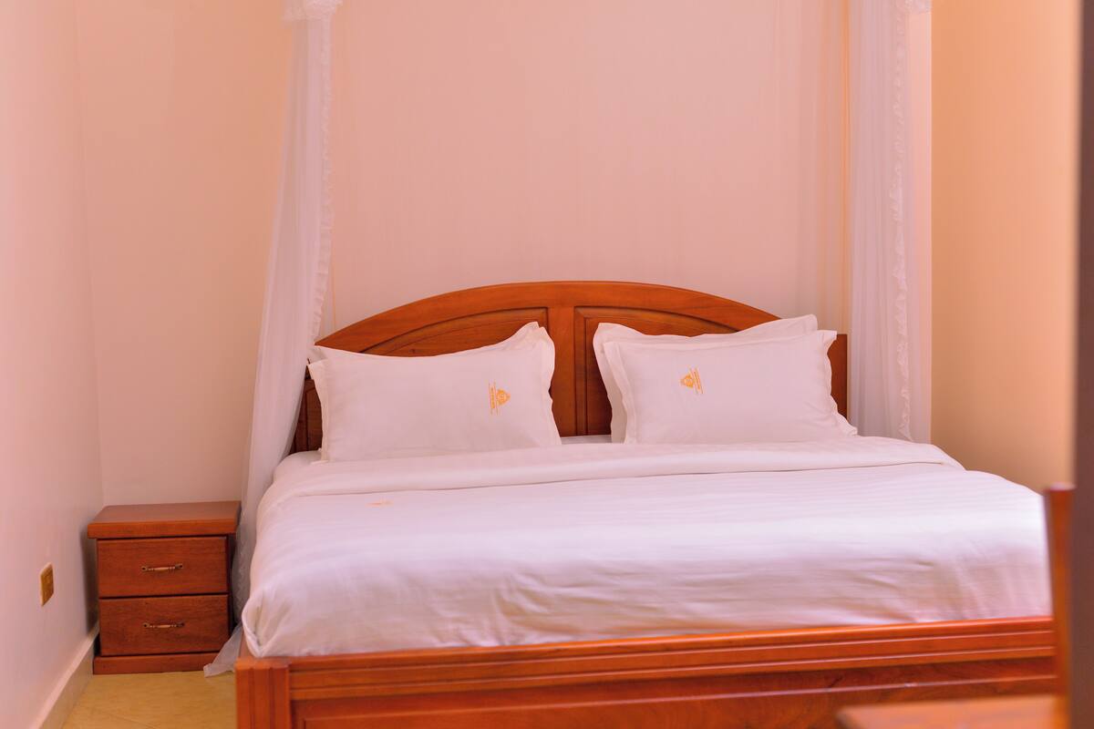 A neatly made bed with white linens and two pillows, a wooden headboard, and a small wooden nightstand with drawers.