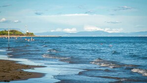 A coastal beach with waves, a lighthouse, and distant mountains.