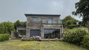 A modern two-story house with a flat roof, large windows, and a covered patio area.