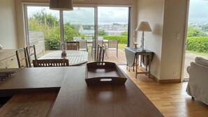 A spacious room with a wooden ceiling, a dining table, chairs, a sofa, and a view through large windows.