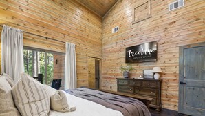 A log cabin bedroom with a bed, a dresser, and a mounted sign that reads "Treevine Vacation Rentals." - Pet-Friendly Forest Retreat for Families & Friends (Broken Bow)