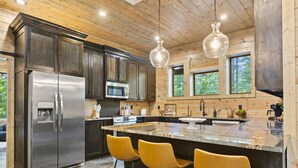 A modern kitchen with stainless steel appliances, a granite island, and yellow chairs. - Pet-Friendly Forest Retreat for Families & Friends (Broken Bow)