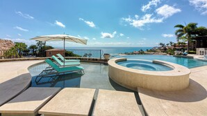 Un espace piscine doté de chaises longues et d’un jacuzzi, offrant une vue panoramique sur l’océan.