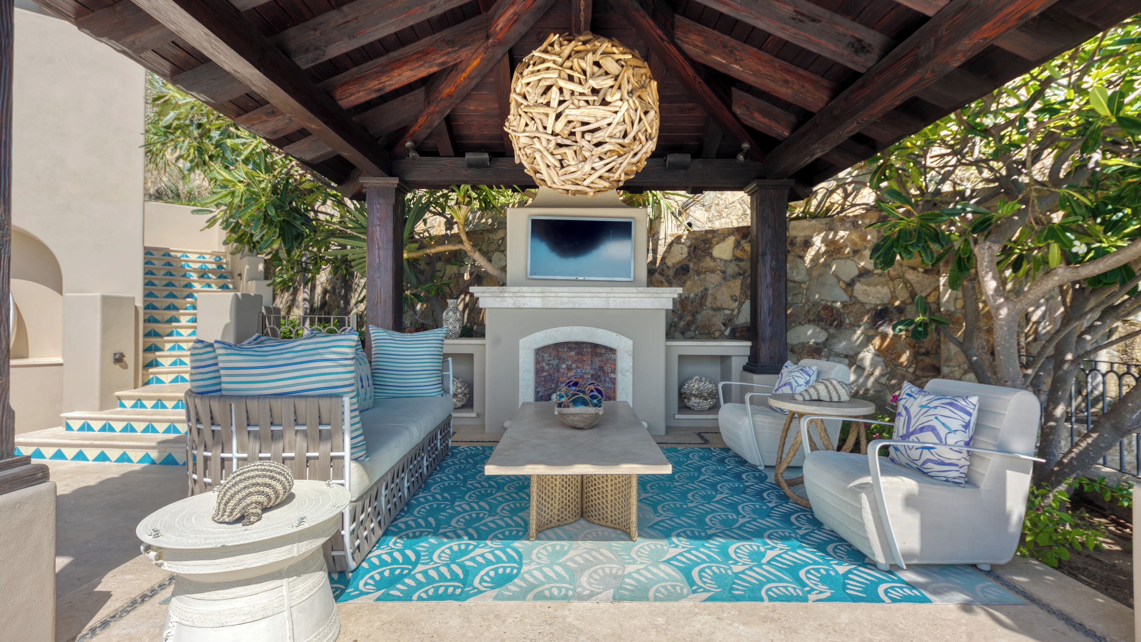 Un espacio de estar al aire libre cubierto con una chimenea de piedra, piso con diseño y un elemento decorativo en el techo.