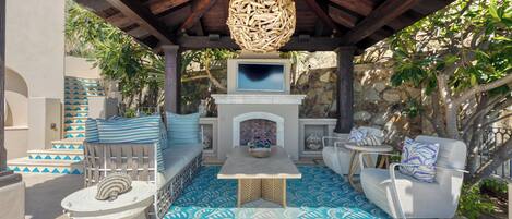 Un espacio de estar al aire libre cubierto con una chimenea de piedra, piso con diseño y un elemento decorativo en el techo.