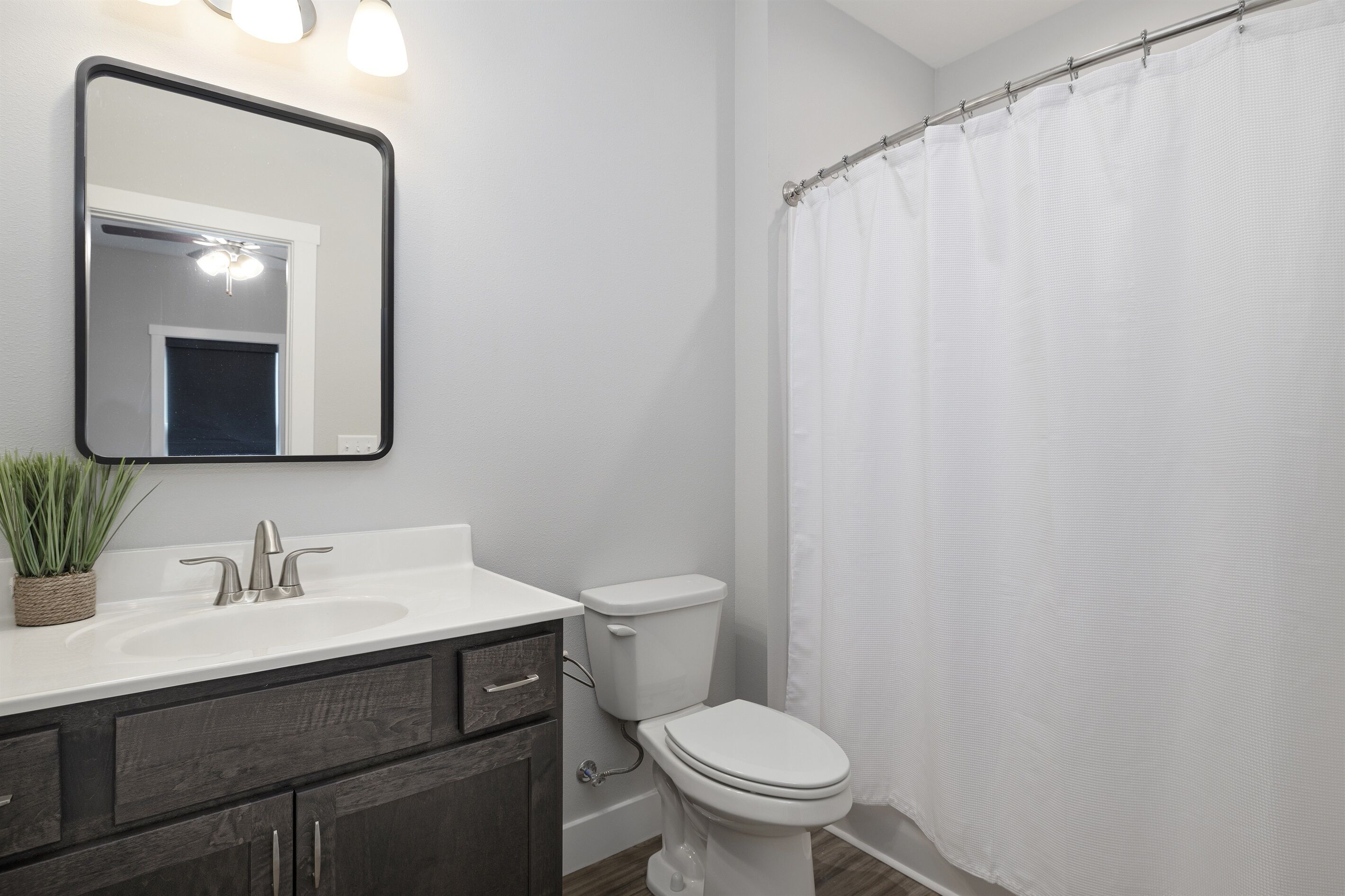 A bathroom with a white sink, dark wooden cabinet, a toilet, and a shower curtain.