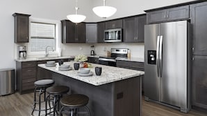 Cocina moderna con armarios oscuros, refrigerador de acero inoxidable, microondas e isla de granito con taburetes de bar.