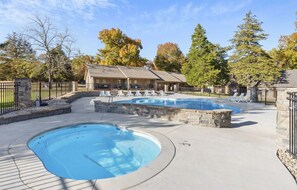 Un espace piscine avec des chaises longues, un bâtiment doté d’un toit en pente et un mur en pierre.