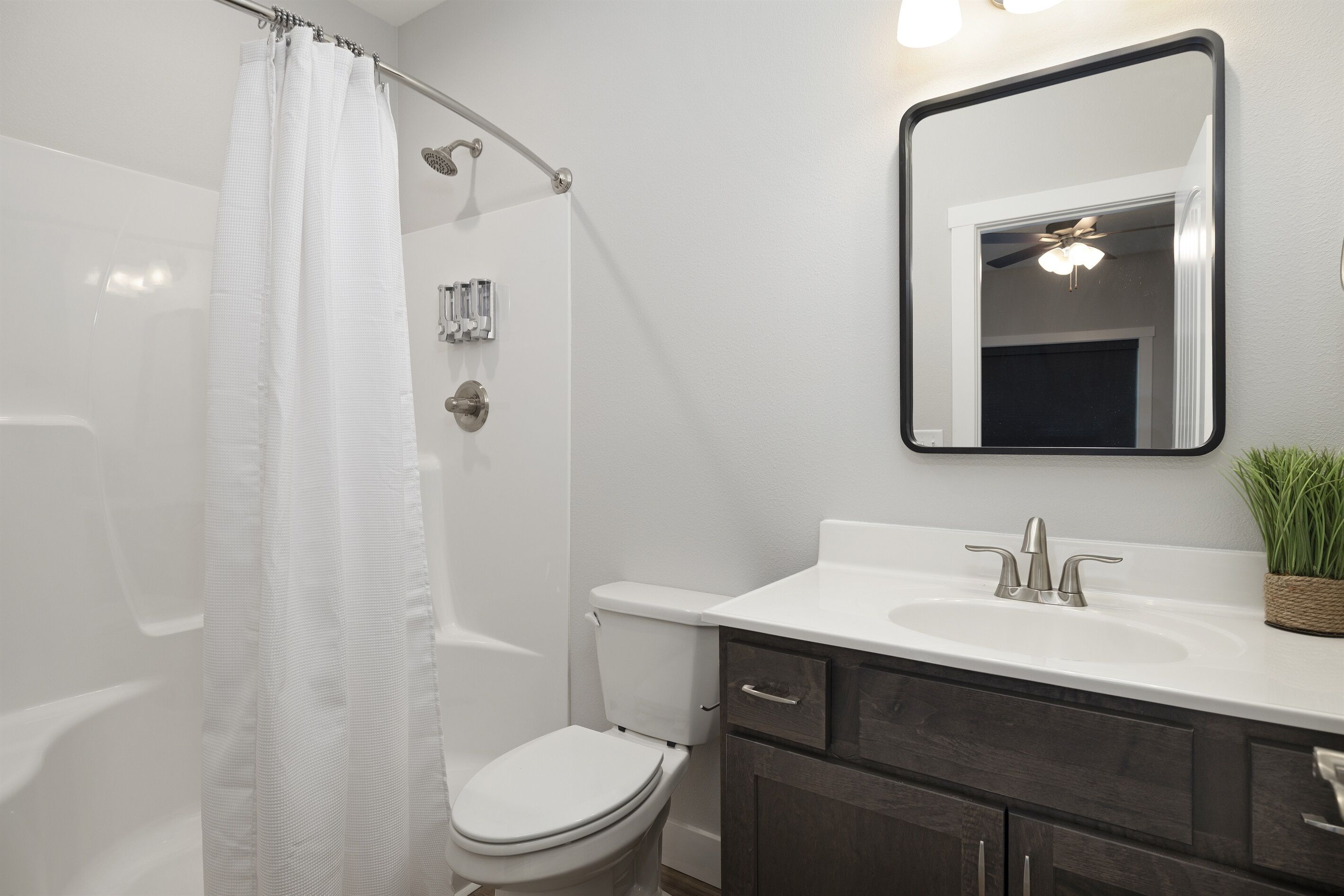 A modern bathroom with a white shower curtain, a toilet, a sink with a mirror above it, and a small potted plant on the sink counter.