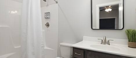 A modern bathroom with a white shower curtain, a toilet, a sink with a mirror above it, and a small potted plant on the sink counter.
