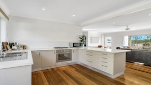 A modern kitchen with white cabinetry, a built-in oven, a microwave, and a sink. - Wooli Waves - Right on the ocean dune. (Wooli)