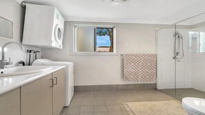 A modern bathroom with a built-in washing machine, a glass shower enclosure, and a window with a view of a building.