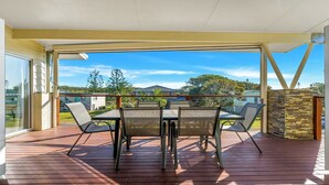 Une terrasse extérieure couverte, avec une table et des chaises, un mur en pierre et une vue sur des maisons et des arbres.