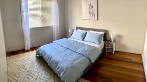 A bedroom with a bed, bedside tables, a nightstand, a window with blinds, and a wall-mounted artwork. - Wooli Waves - Right on the ocean dune. (Wooli)