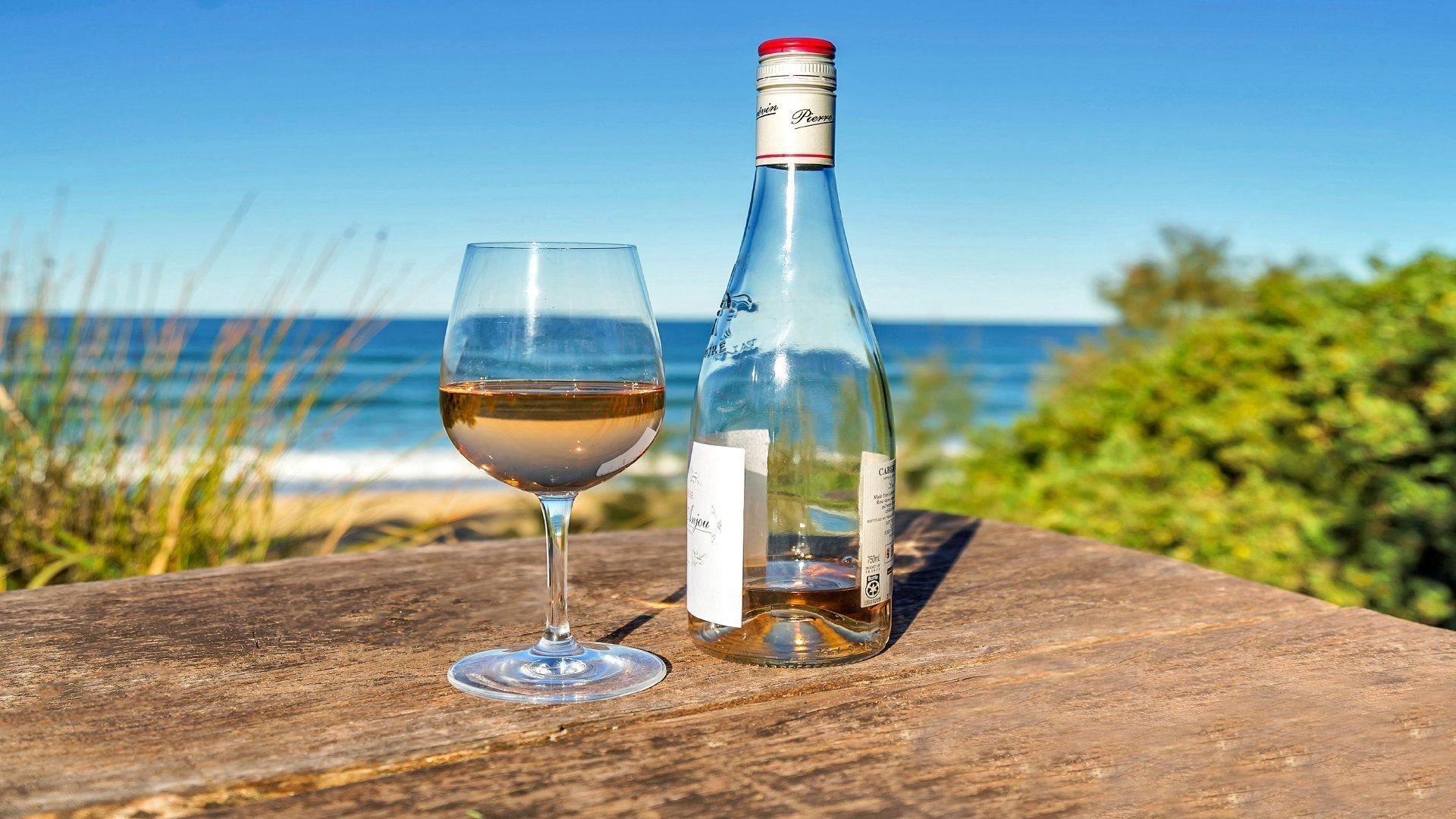 Een fles en een glas witte wijn op een houten oppervlak met uitzicht op de oceaan.