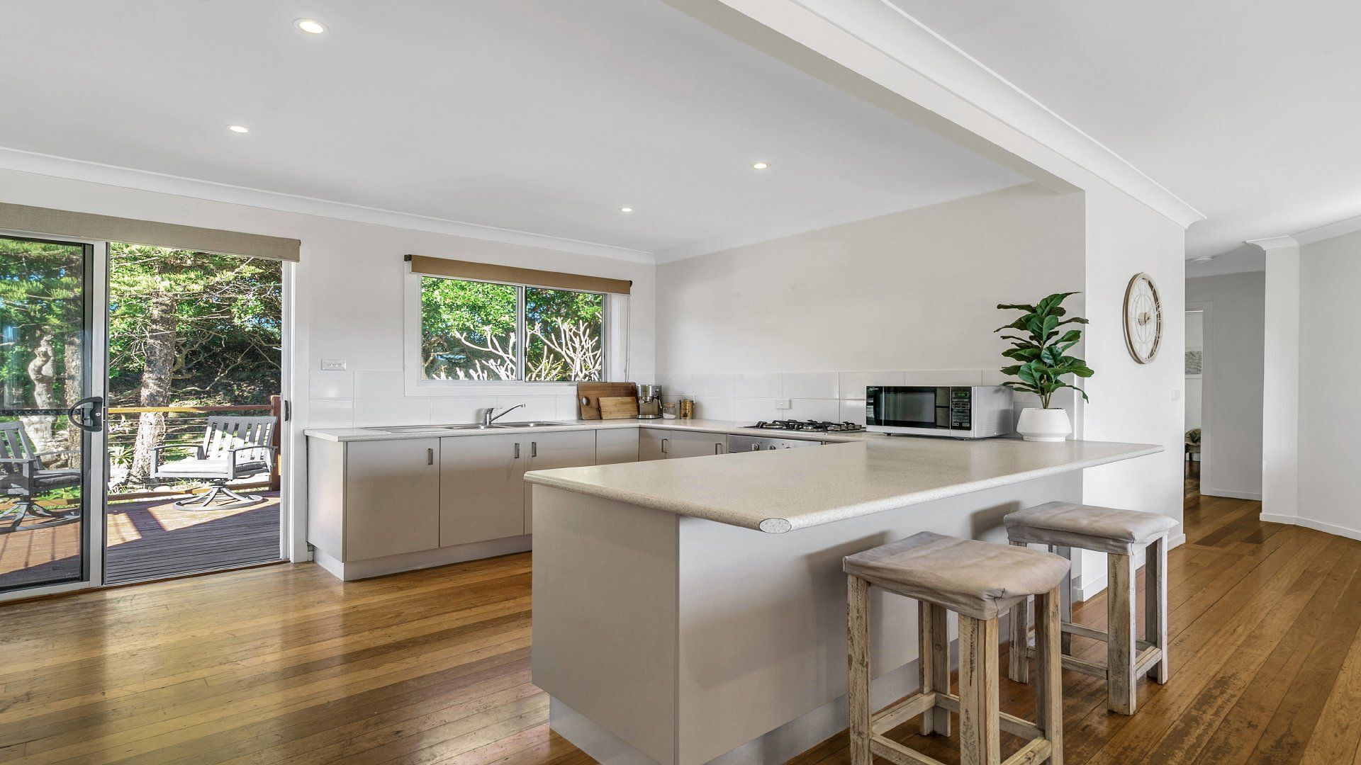 A modern kitchen with a central island, wooden flooring, and a view of the outdoors.