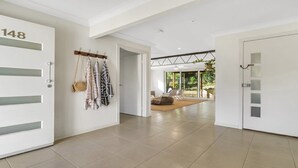 A hallway with a white door labeled '148', a coat rack with hanging items, and a view into a room with a large window and a plant. - Wooli Waves - Right on the ocean dune. (Wooli)