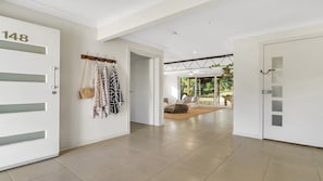 A hallway with a white door labeled '148', a coat rack with hanging items, and a view into a room with a large window and a plant. - Wooli Waves - Right on the ocean dune. (Wooli)