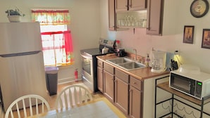 Cocina compacta con refrigerador, estufa, pileta y microondas. Incluye una mesa de comedor con sillas, una ventana con cortinas y un extintor en el suelo.