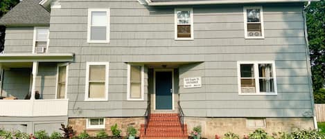 A two-story house with a front porch, a brick entrance, and a sign indicating the entrance to apartments 2 and 3.