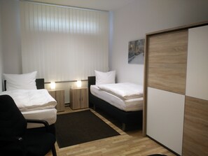 A hotel room with two beds, a desk, a chair, and a wardrobe.