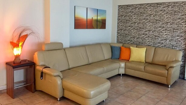 En stue med en beige hjørnesofa, et lille bord med en lampe, og et kunstværk på væggen.