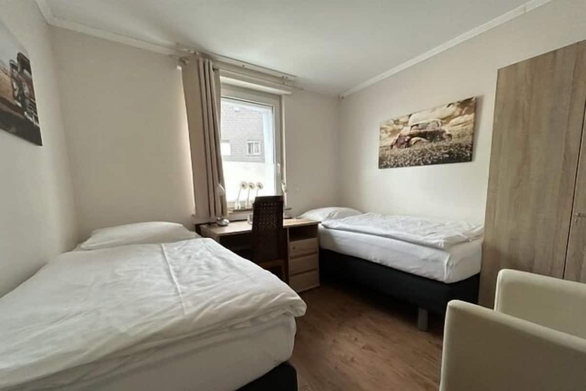 Ein kleines, sauberes Zimmer mit zwei Einzelbetten, einem Schreibtisch und einem Stuhl.