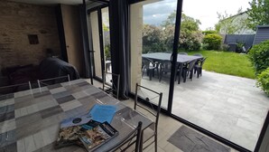 A modern patio area with a glass door leading to a garden. There is a table with a placemat and a few items on it. - Cosy Maison Familiale 10 Personnes (Péaule)