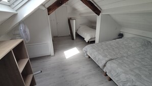 A bedroom with a sloped ceiling, wooden beams, a bed with patterned bedding, a bedside table, and a fan. - Cosy Maison Familiale 10 Personnes (Péaule)