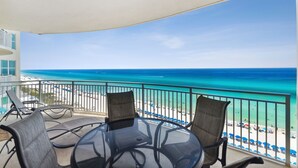 A balcony with a glass table and chairs, overlooking a beach with clear blue water and a sandy shore. - Aqua 802 Oceanfront/Hi+Clean Standard/Wifi/Beach Chairs (Panama City Beach)