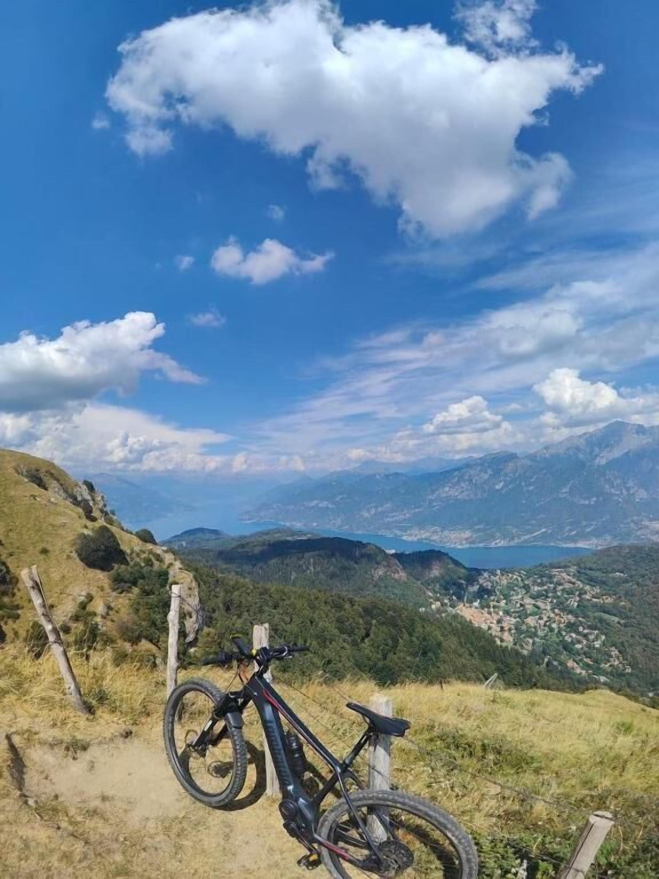 Una bicicleta de montaña aparcada en un sendero de tierra, con una vista panorámica de un valle y montañas al fondo.