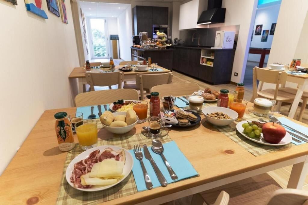 Une table de petit-déjeuner avec divers aliments et boissons, une cuisine en arrière-plan et un coin repas avec des chaises.