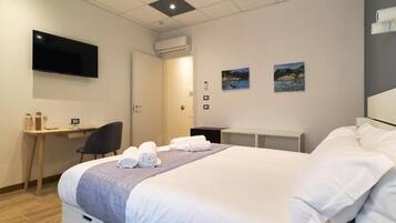 A hotel room with a bed, a desk, a chair, a TV, and two paintings on the wall.