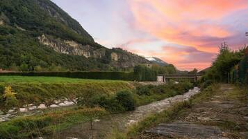 Une rivière qui traverse une vallée, avec un pont, et qui est bordée d’une végétation luxuriante et de collines.