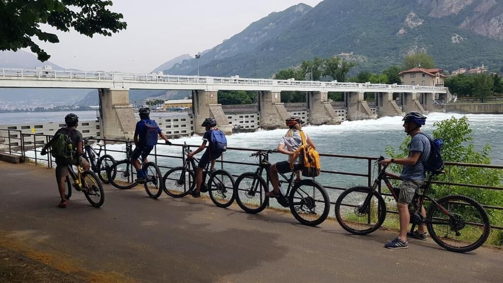 Un groupe de cyclistes sur un pont, avec une rivière et des montagnes en arrière-plan.