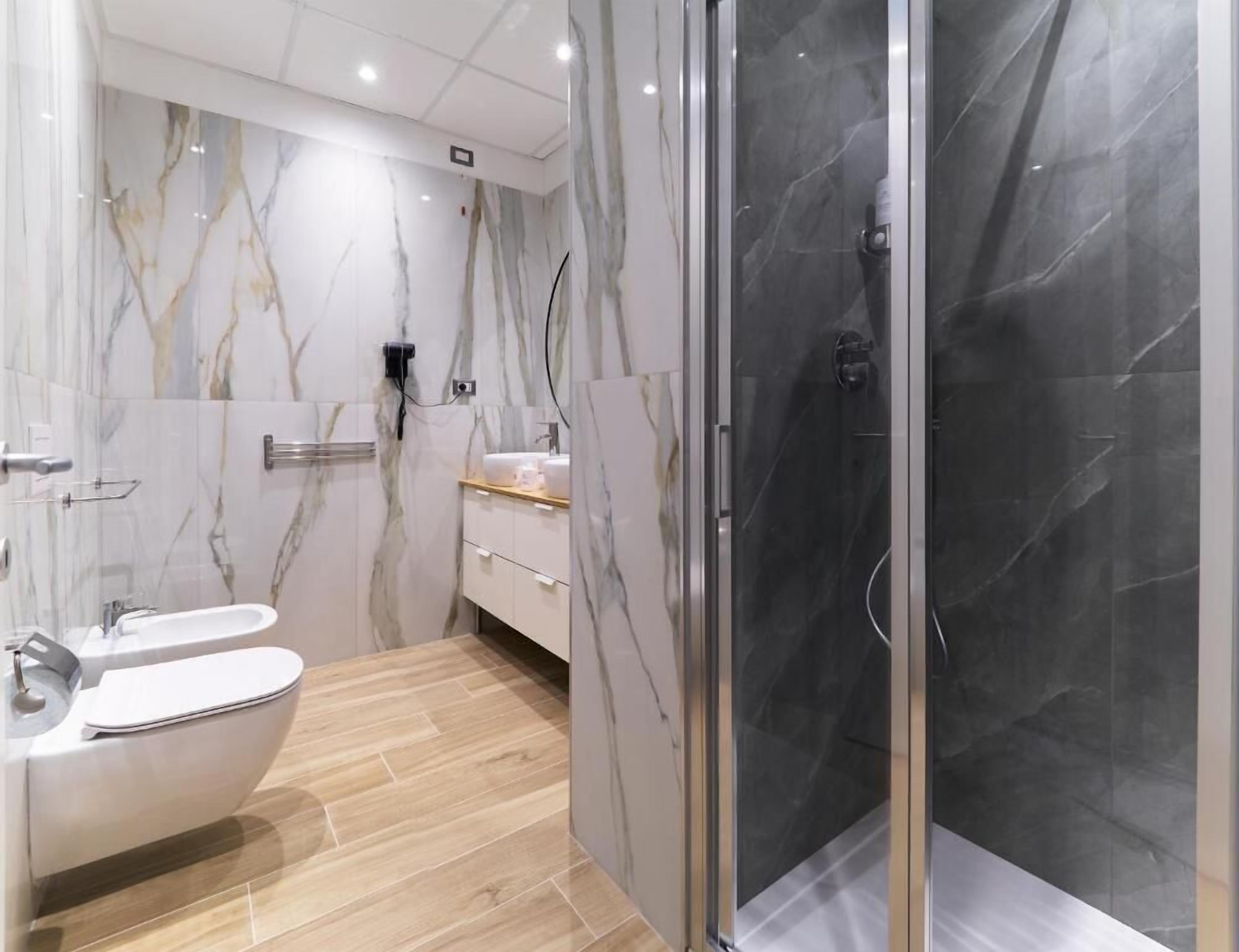 A modern bathroom with a marble vanity, a toilet, and a glass-enclosed shower.