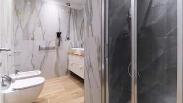 A modern bathroom with a marble vanity, a toilet, and a glass-enclosed shower.