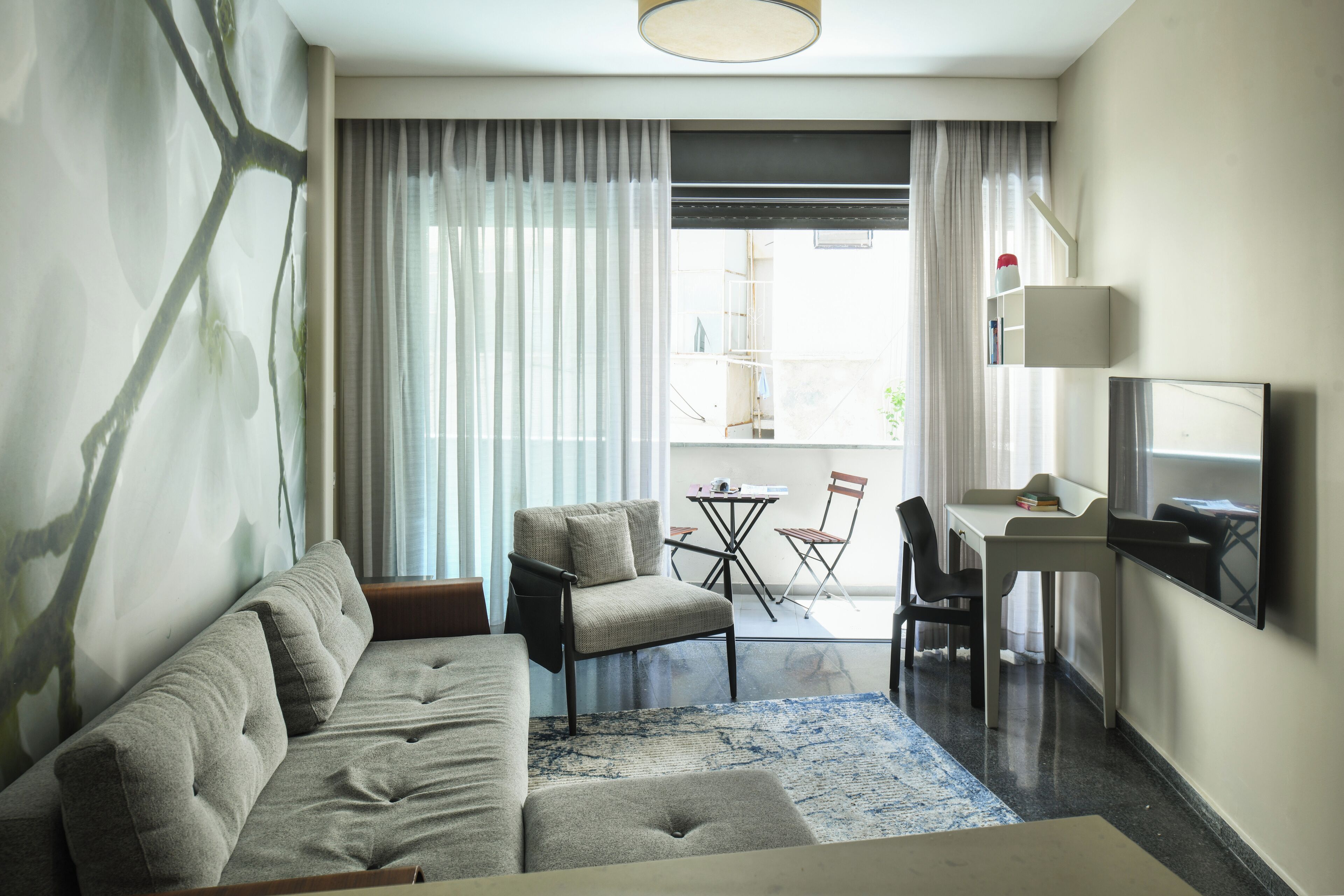 Une chambre d’hôtel moderne équipée d’un canapé, d’une petite table, d’une chaise, d’un téléviseur et offrant une vue sur l’extérieur.
