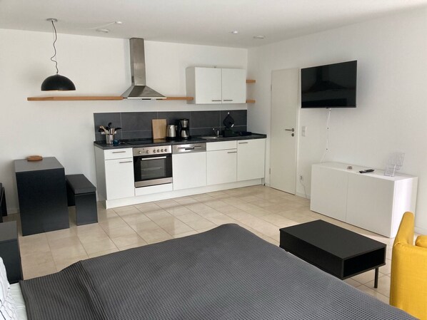 A modern, compact bedroom with a bed, bedside tables, a TV, and a kitchenette.